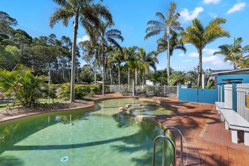 a swimming pool with palm trees and a bench at White Crest Apartments in Hervey Bay