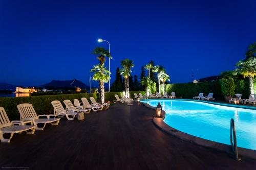 a pool at night with lounge chairs and palm trees at Hotel Villa e Palazzo Aminta in Stresa