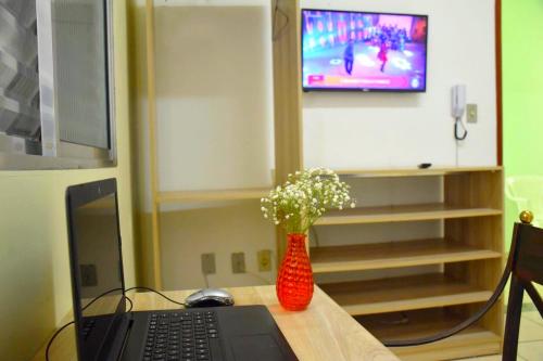 a desk with a laptop and a vase of flowers at Pousada Tokyo Plaza in Mogi das Cruzes