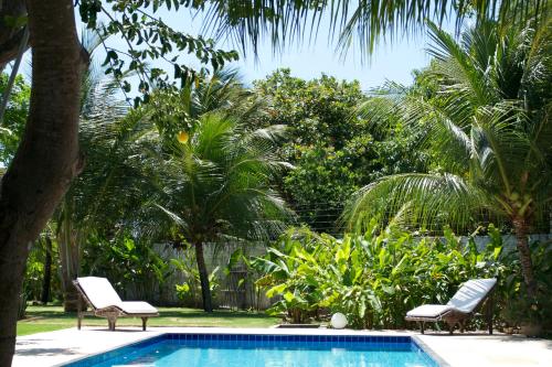 a swimming pool with two chairs and palm trees at Refugios Parajuru - Casa Verde in Parajuru