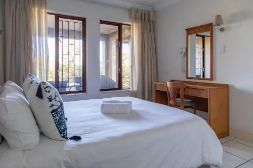 a bedroom with a white bed with a desk and windows at Castleton Plettenberg Bay in Plettenberg Bay