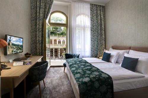 カルロヴィ・ヴァリにあるASTORIA Hotel & Medical Spaのベッド、デスク、窓が備わるホテルルームです。