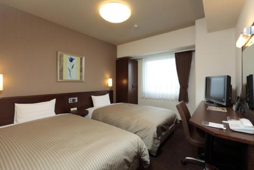 a hotel room with two beds and a desk and a television at Hotel Route-Inn Toyotajinnaka in Toyota