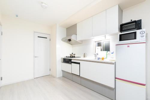 a white kitchen with a refrigerator and a microwave at Villa de Class in Osaka