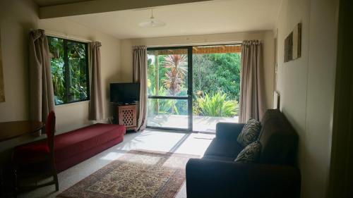 a living room with a red couch and a sliding glass door at Wharepuke Subtropical Accommodation in Kerikeri