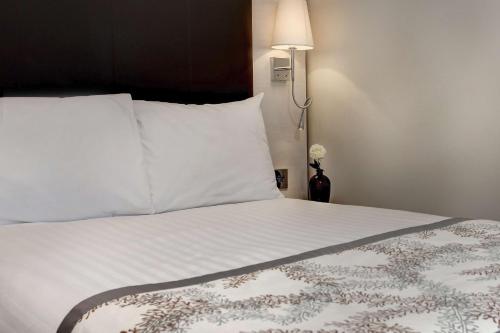 a bedroom with a bed with white sheets and a lamp at Best Western Chiswick Palace & Suites London in London