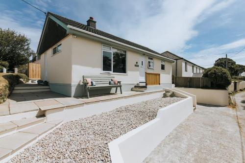 a white house with a bench on a gravel driveway at Sunset in Newquay