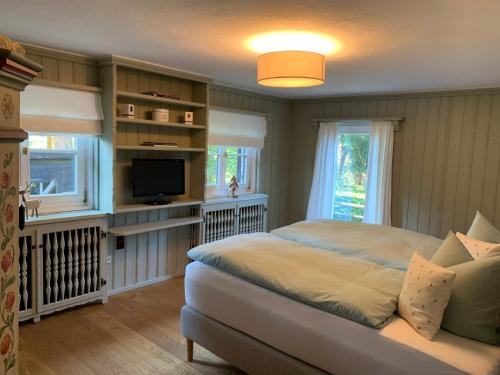 a bedroom with a bed and a tv and windows at Traumhaftes Ferienhaus direkt am Tegernsee in Rottach-Egern