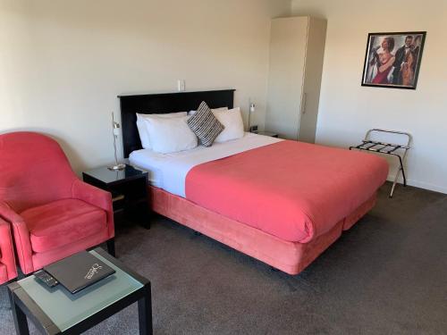 a bedroom with a large bed and a red chair at Salerno Motel Apartments in Christchurch