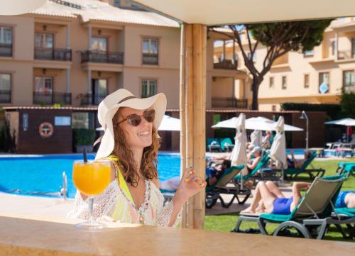 a woman sitting at a table with a drink at Aqua Pedra Dos Bicos Design Beach Hotel - Adults Only in Albufeira