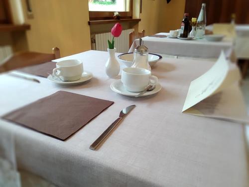 a table with cups and saucers and a flower on it at Hotel Garnì Miramonti in Falcade