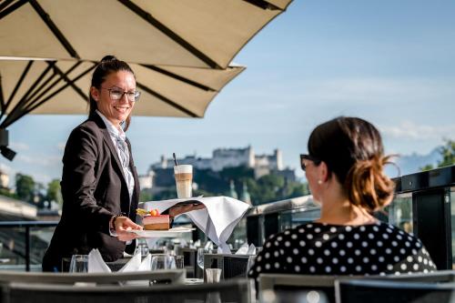 a woman holding a plate of food on a table at IMLAUER HOTEL PITTER Salzburg in Salzburg