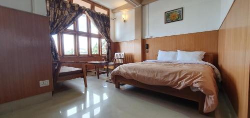 a bedroom with a bed and a desk and a window at Hotel The Oak in Tawang