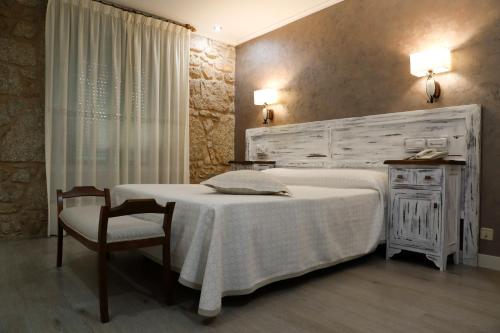 a bedroom with a white bed and a chair at Pensión O Prouso in San Mamede de Carnota