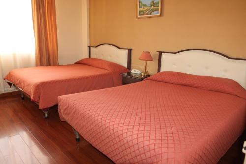two beds in a hotel room with orange sheets at Hotel Luxor in Cochabamba