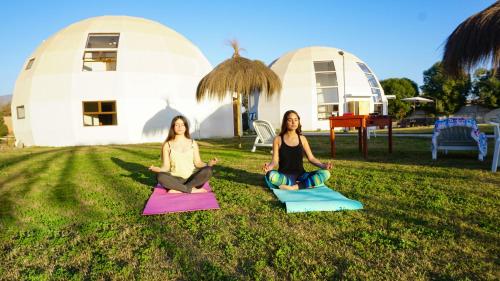 Dos mujeres sentadas en la hierba haciendo yoga frente a las cúpulas en Domos Dream, en La Serena