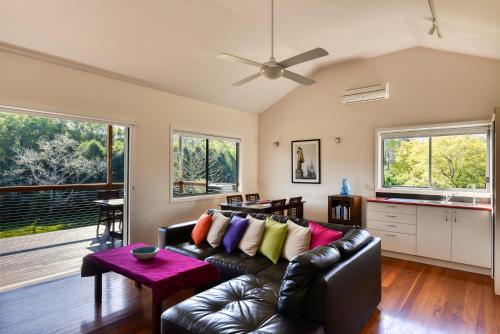a living room with a black leather couch with colorful pillows at Afterglow Cottages in Bellingen