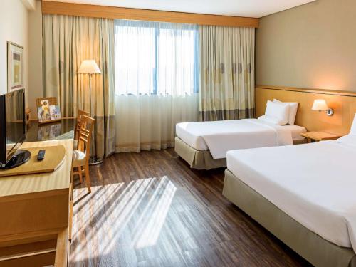 a hotel room with two beds and a television at Novotel Sao Paulo Center Norte in Sao Paulo