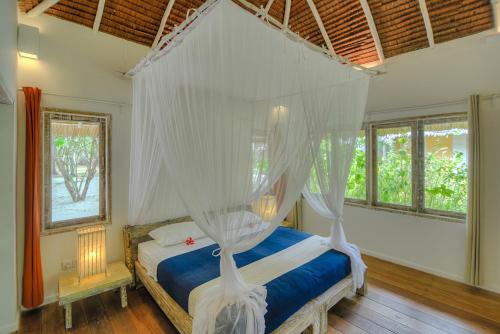 Trikora Beach Club and Resort في تيلوكباكاوْ: غرفة نوم مع سرير مظلة مع ناموسيات بيضاء