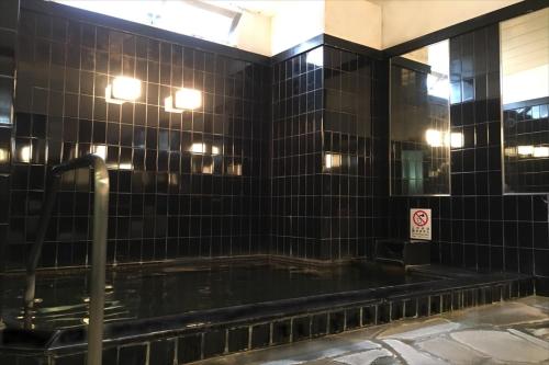 a black tiled bathroom with a hot tub at Green Rich Hotel Iwakuni Ekimae (Artificial hot spring Futamata Yunohana) in Iwakuni