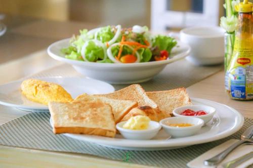a white plate with toast and a salad and a plate of food at Crystal Jade Hotel in Rayong