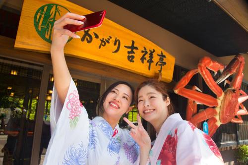 deux femmes debout devant un restaurant tenant un téléphone portable dans l'établissement Yamanaka Onsen Kagari Kisshotei, à Kaga