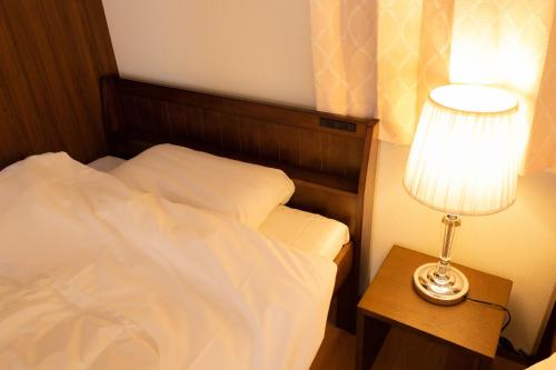 a bedroom with a bed and a table with a lamp at Guesthouse Hajimari in Kashihara