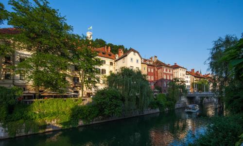 a river in a city with buildings and a boat at Kollmann Rooms and Apartments in Ljubljana