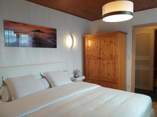 - une chambre avec un lit blanc et une armoire en bois dans l'établissement Chambres du Jardin Fleuri, à Saint-Aubin-lès-Elbeuf