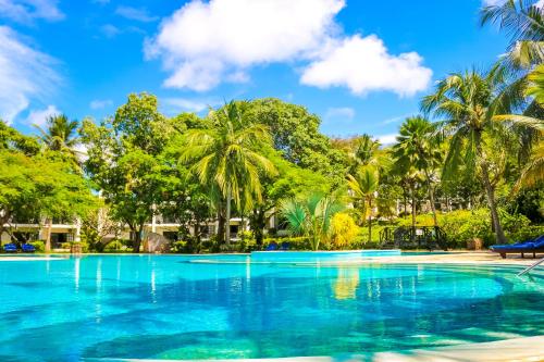 a large swimming pool with palm trees in the background at Diani Sea Resort - All Inclusive in Diani Beach