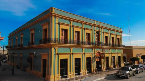 a yellow and blue building with cars parked in front of it at Hotel Santa Elena in El Fuerte