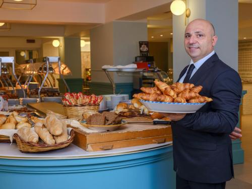 a man in a suit holding a plate of bread at Hotel Antares in Letojanni