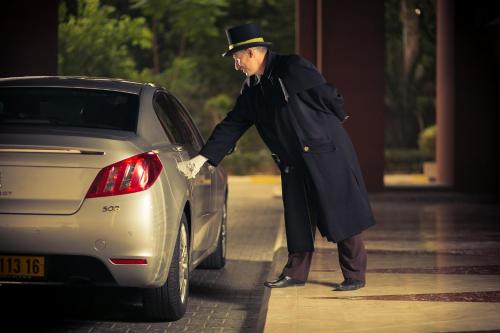 an older man in a coat and top hat standing next to a car at Sofitel Algiers Hamma Garden in Alger
