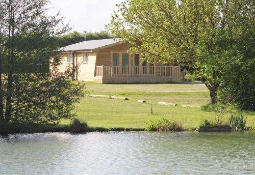a house with a lake in front of it at Woodpecker Lodge - Brook Meadow - sleeps 4 plus 2 - no pets in Market Harborough