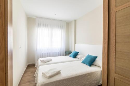 two beds in a white room with blue pillows at Apartamento Rosaleda in Melide