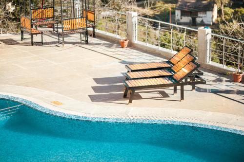 2 sedie in legno sedute accanto alla piscina di Sea Hawk - Luxury Hill Resort 4 mins from Bhimtal Lake a Bhimtal