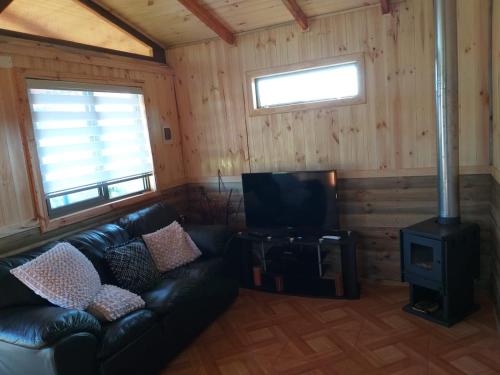 a living room with a leather couch and a stove at Cabañas Don Tito in Buchupureo