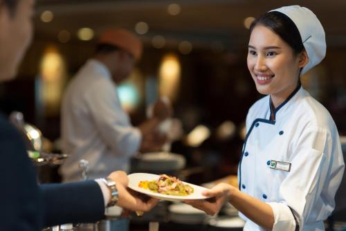 a woman is holding a plate of food at The Emerald Hotel in Bangkok