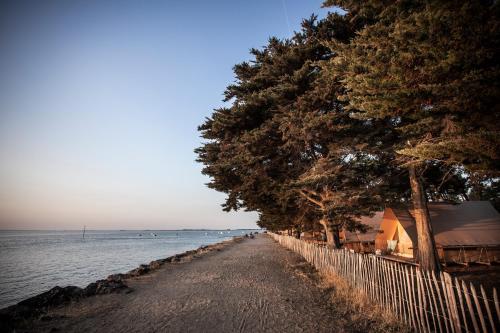 une plage avec des arbres et une clôture à côté de l'eau dans l'établissement Huttopia Noirmoutier, à Noirmoutier-en-l'lle