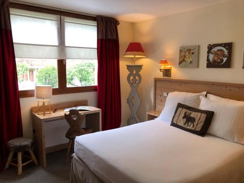 a bedroom with a bed and a desk and a window at Hôtel Restaurant La Tourmaline in Aime La Plagne