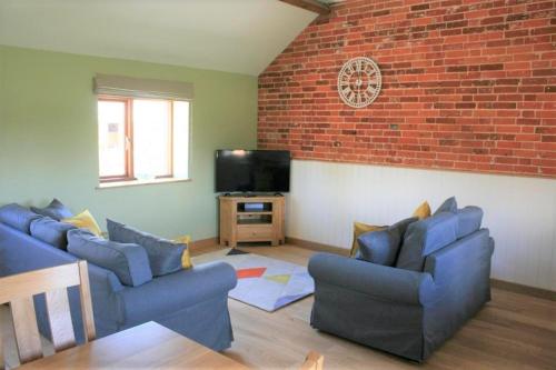 a living room with two blue couches and a tv at Blashford Manor Holiday Cottage - The Dartmoor Cottage in Ellingham