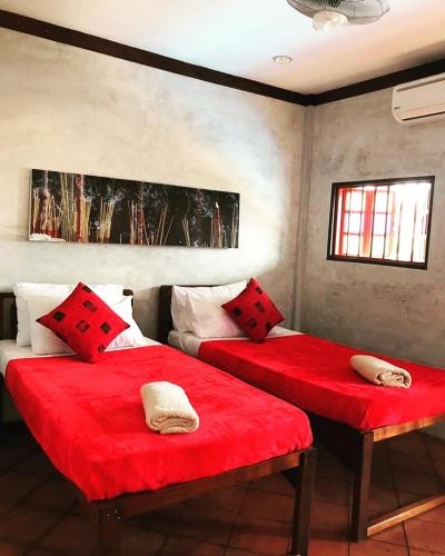 two beds in a room with red sheets and pillows at tanabendang banglos in Pantai Cenang
