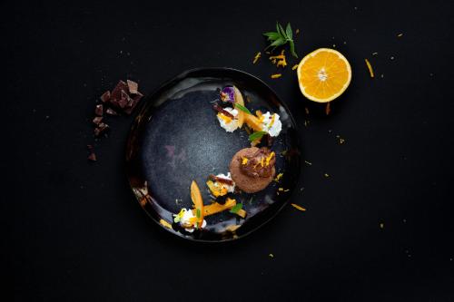 a black plate of food with an orange slice at De Kombuys in Oudtshoorn