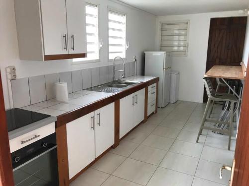 a kitchen with white cabinets and a sink and a refrigerator at LeSaintCyr in Sainte-Rose