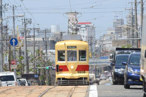 a yellow tram driving down a busy city street at Hotel Arc Riche Toyohashi in Toyohashi