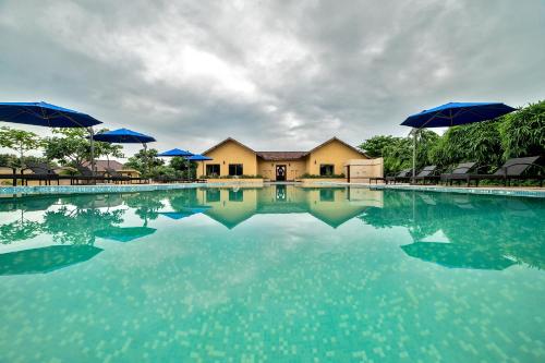 une grande piscine d'eau avec des parasols en face d'une maison dans l'établissement WelcomHeritage Tadoba Vanya Villas Resort & Spa, à Kolāra