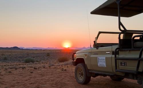 a truck parked in the desert with the sunset in the background at Twyfelfontein Country Lodge in Twyfelfontein
