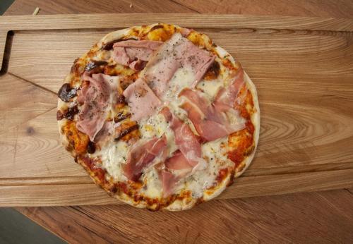 a pizza with ham and cheese on a wooden table at Haus 4 Montafon by Pferd auf Wolke in Gaschurn