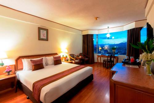 a hotel room with a bed and a desk and a window at Duangtawan Hotel Chiang Mai -SHA Extra Plus in Chiang Mai