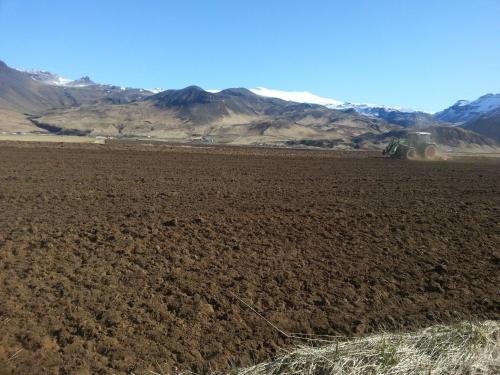 a tractor cultivating a field with mountains in the background at Ásólfsskáli Cottage in Ásólfsskáli